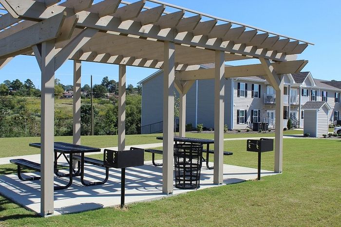 Charming outdoor picnic area with pergola, surrounded by lush green grass, perfect for gatherings at modern apartment complex.