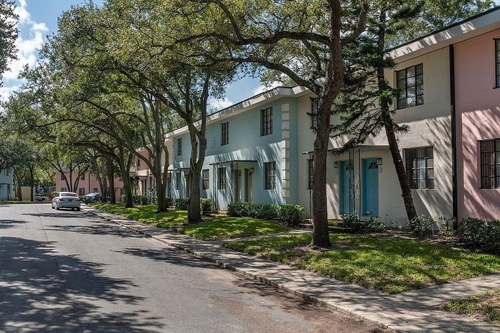 Charming neighborhood view showcasing pastel-colored townhouses nestled under leafy trees, creating a serene and inviting atmosphere.