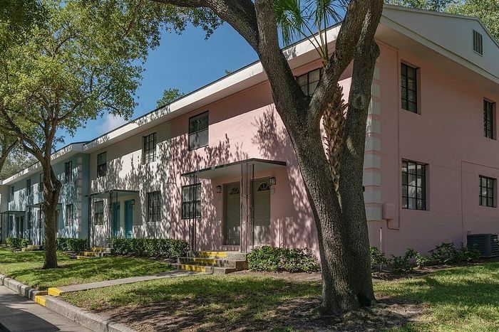 Charming apartment building with pastel-colored exteriors set against a lush green landscape and mature trees.