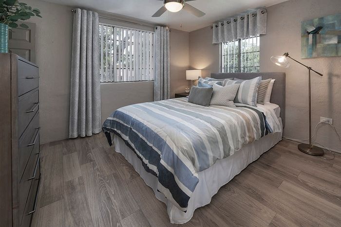 Inviting bedroom with modern decor, featuring striped bedding, a chic floor lamp, and large windows providing abundant natural light.