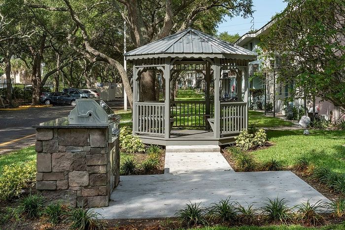Charming garden view with a picturesque gazebo and stone barbecue area surrounded by lush greenery, perfect for outdoor relaxation and entertaining.
