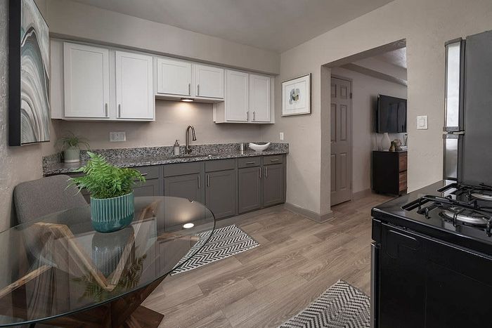 Modern kitchen with elegant gray cabinets, granite countertops, and sleek glass dining table, offering a stylish and functional living space.