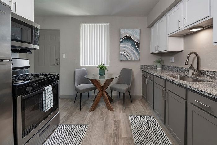 Contemporary kitchen with sleek stainless steel appliances, elegant wood flooring, and a chic dining nook with a glass table.