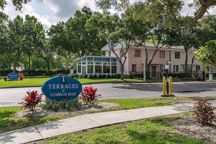 Charming view of Terraces at Clearwater Beach showcasing lush green landscaping, modern architecture, and a welcoming entrance sign.