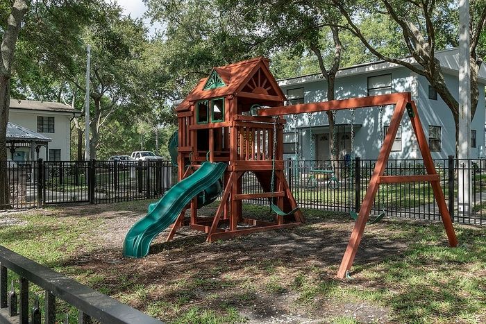 Charming playground with a wooden playset and slide nestled among mature trees, offering a perfect family-friendly community space.