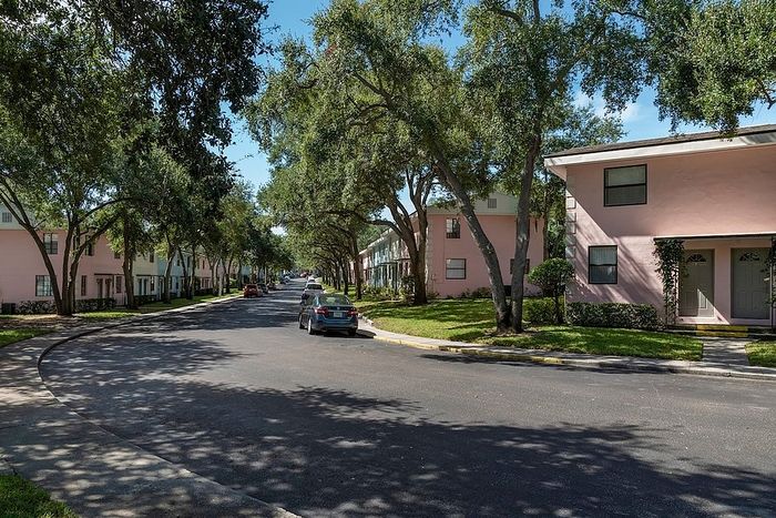 Charming residential neighborhood featuring pastel-colored buildings, lined with lush trees on a sunny day.