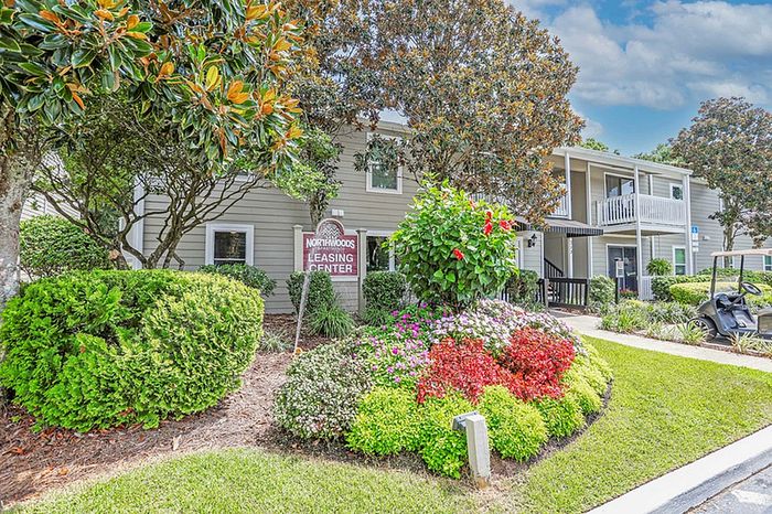Charming apartment building surrounded by lush greenery and colorful flower beds, showcasing a serene and inviting environment.