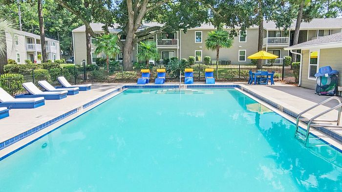 Inviting apartment community pool area with comfortable lounge chairs, vibrant umbrellas, and lush greenery, offering a perfect spot for relaxation and leisure.