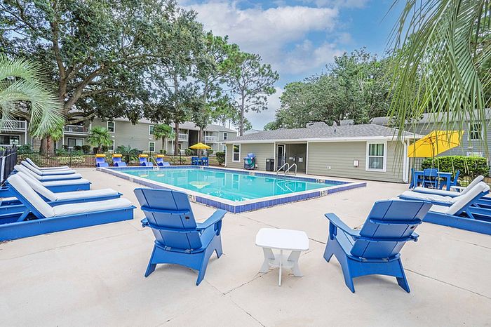 Inviting outdoor pool area with modern blue lounge chairs, surrounded by lush greenery and vibrant yellow umbrellas.