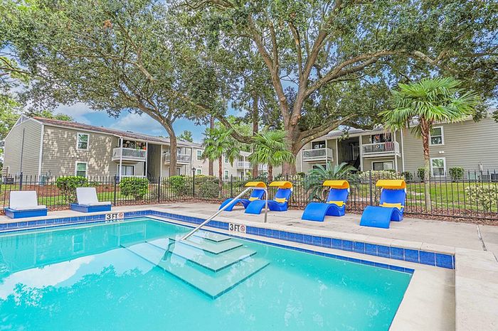 Inviting apartment complex with a sparkling outdoor pool, surrounded by vibrant lounge chairs and lush greenery, perfect for relaxation.