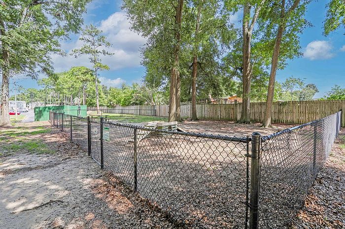 Inviting outdoor space featuring a spacious, fenced dog park surrounded by lush green trees, perfect for pet-friendly living.