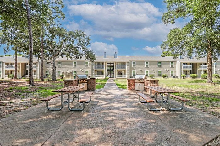 Inviting apartment complex showcasing lush green surroundings, picnic tables, and outdoor grill area against a backdrop of well-maintained buildings.