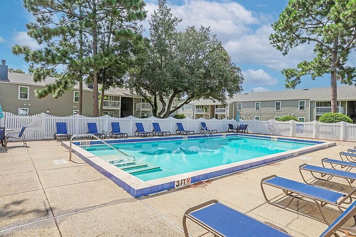 Inviting outdoor pool area with comfortable lounge chairs, surrounded by lush trees and modern apartment buildings, perfect for relaxation.