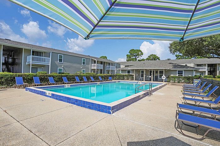 Inviting apartment community with a sparkling resort-style pool, surrounded by blue loungers and lush landscaping.