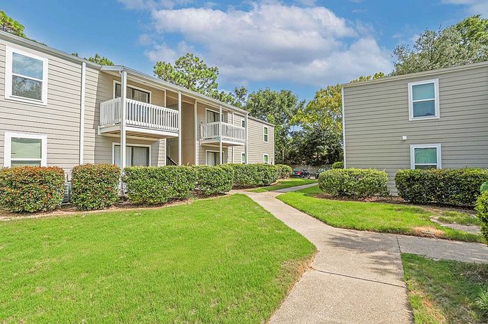 Charming apartment exterior with well-manicured landscaping, private balconies, and inviting walkway in a serene setting.