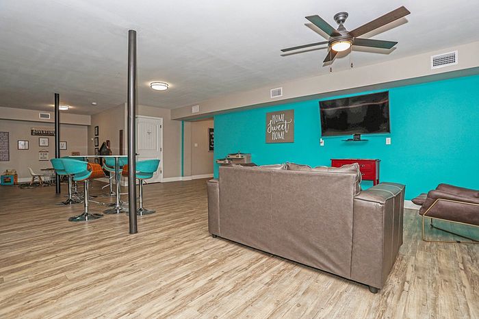 Modern open space with sleek hardwood flooring, vibrant teal accent wall, and comfortable brown leather seating area, featuring a mounted TV and stylish ceiling fan.