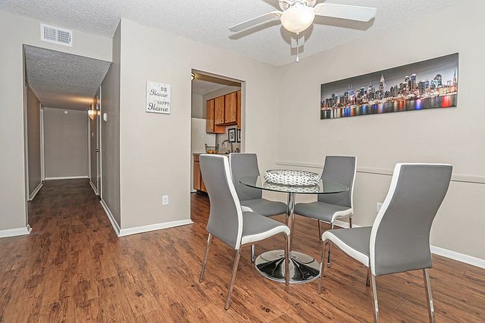 Modern dining area with stylish grey chairs and glass table, featuring elegant wood flooring and a vibrant cityscape artwork.