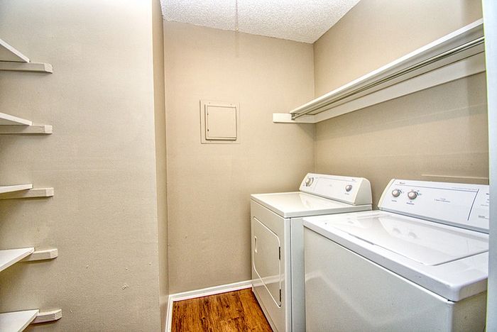 Modern laundry room with sleek washer and dryer, featuring ample shelving and stylish wood flooring.