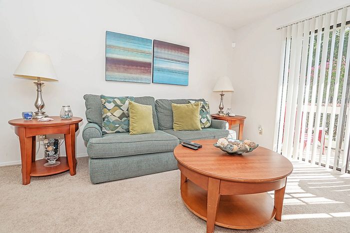 Bright and inviting living room with modern decor, featuring a comfortable sofa, stylish coffee table, and elegant side tables with lamps, complemented by artwork and natural light streaming through vertical blinds.