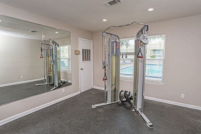 Modern fitness room with versatile workout machine and large mirror overlooking a bright window with pool view.