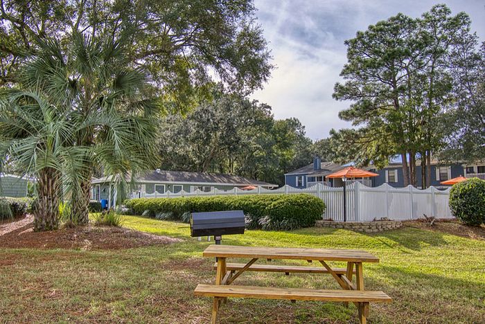Charming outdoor space with picnic table, grill, and lush greenery, perfect for social gatherings.