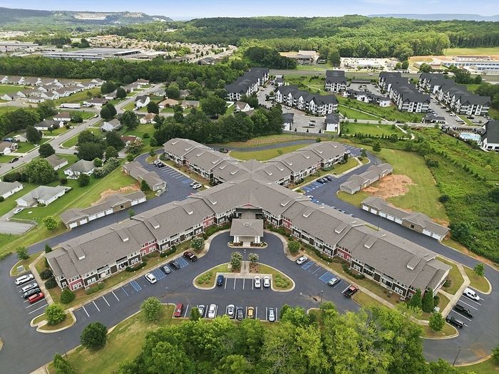 Aerial view of sprawling apartment complex surrounded by lush greenery and scenic landscape, showcasing modern architecture and ample parking.