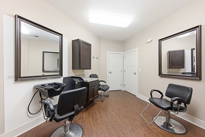 Elegant salon suite with sleek black styling chairs, large mirrors, and warm wood flooring, offering a cozy and professional ambiance.