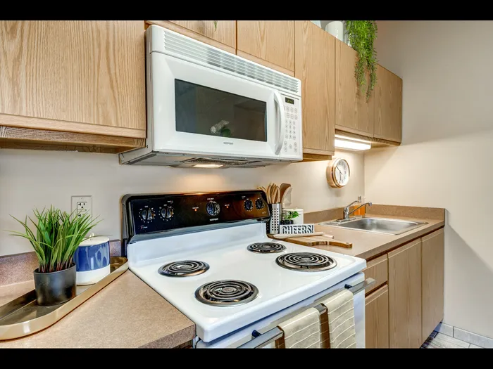 Close-up of white electric range and honey-colored cabinetry  in apartment at University Gate | Erie, PA Apartments.