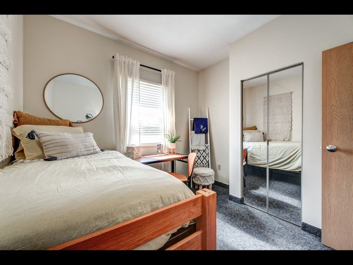 Staged bedroom with bed, desk & chair, mirrored sliding doors on closet, and window letting in natural light in apartment at University Gate | Erie, PA Apartments.