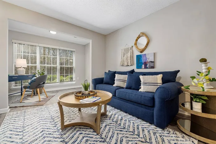 Living room with blue couch next to sun room with desk