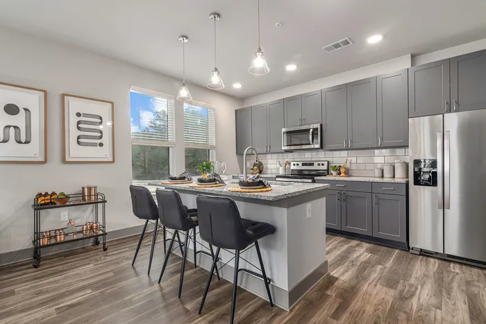 Birmingham, AL, Apartments - Tributary Rise - Culinary-Inspired Kitchen with Hardwood-Style Flooring, Granite Countertops, Breakfast Bar with Bar-Style Chairs, Whirlpool Appliances, Windows with Blinds, and Pendant Lighting.