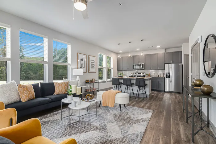 Pet-Friendly Apartments in Birmingham, AL - Tributary Rise - Open-Concept Living Room with Hardwood-Style Flooring, Area Rug, Couch, Coffee Table, Armchairs, Windows with Blinds, and View of Kitchen Area.