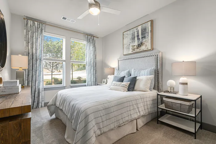 Apartments in Birmingham For Rent - Tributary Rise - Bedroom With Carpeted Flooring, Large Bed, Nightstands With Lamps, Dresser, Ceiling Fan With Light, And Windows With Blinds And Coverings.