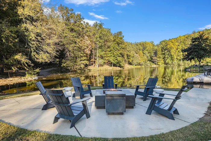 Studio Apartments in Birmingham, AL - Tributary Rise - Lakeside Firepit with Wooden Lounge Seats and View of Lush Trees.