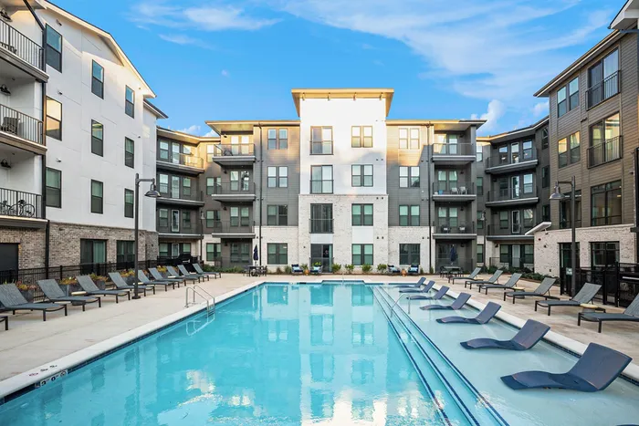 2-Bedroom Apartments in Birmingham, AL - Tributary Rise - Resort-Style Saltwater Pool with In-Pool and Pool-Side Lounge Seats, and View of Apartment Buildings.