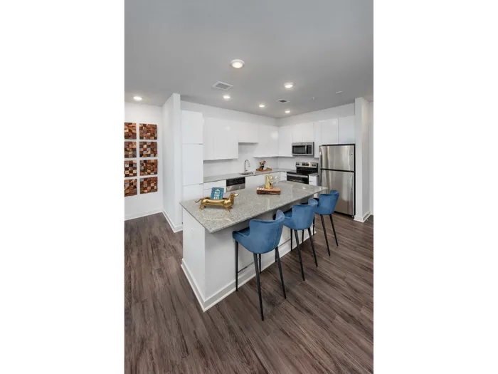 Studios in Atlanta, GA - Spectrum on Spring - Contemporary Open Kitchen with Wood-Style Plank Flooring, White Cabinetry, Stainless Steel Appliances, Granite Countertops, Large Island with Blue Bar-Style Chairs