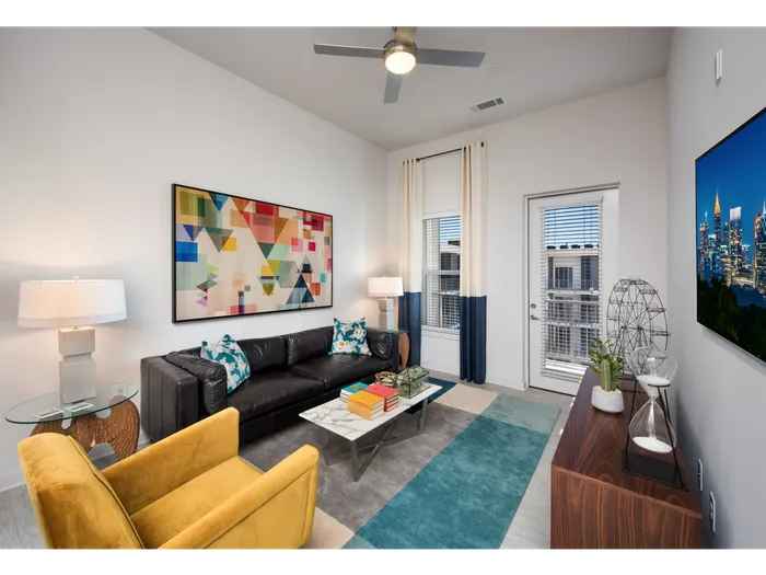Dog Friendly Apartments in Atlanta, GA - Spectrum on Spring - Furnished Living Room with Leather Couch, Yellow Armchair, Glass-Top Side Tables with Lamps, Wooden Cabinet, Mounted TV, white Walls, Ceiling Fan, Window, and Door with Access to Balcony
