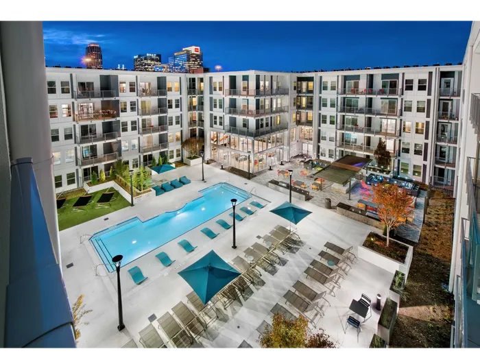 Luxury Apartments for Rent in Atlanta, GA - Spectrum on Spring - Nighttime View of Resort-Style Pool Surrounded by Apartment Buildings With Lounge Chairs, Blue Umbrellas, and BBQ Area with Grill Stations