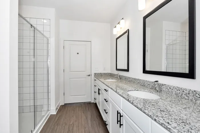 Athens, AL, Apartments Near Madison - Gateway Village at Swan Creek - Spacious Bathroom With Double-Sink Vanity, Granite Countertop, Framed Mirrors, Modern Lighting, and Glass-Enclosed Tile Shower.
