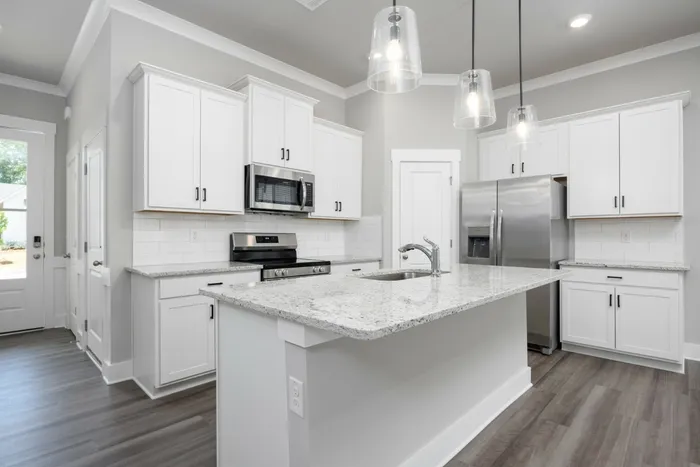 2-Bedroom Homes for Rent in Opelika, AL - Champions Square - Gourmet Kitchen with Luxury Vinyl Plank Flooring, Kitchen Island, Pendant Lights, Granite Countertops, Ceramic Tile Backsplash, White Cabinetry, and Stainless-Steel Appliances.