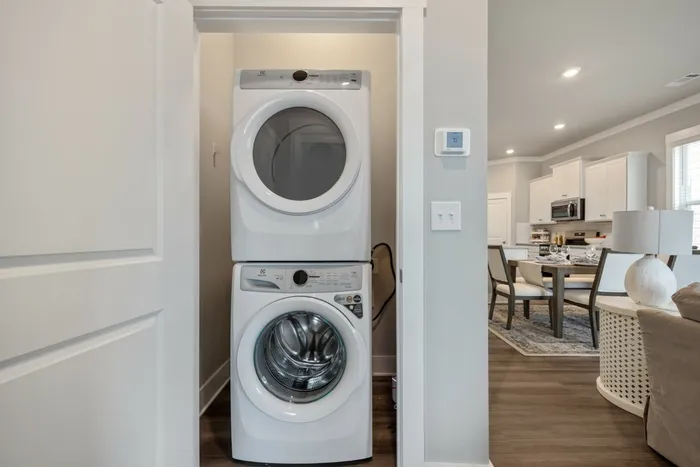 2-Bedroom Homes for Rent in Opelika, AL - Champions Square - Laundry Closet With Stacked Washer And Dryer, Wood Style Flooring, Recessed Lighting, And White Trim Near Open Living Area.