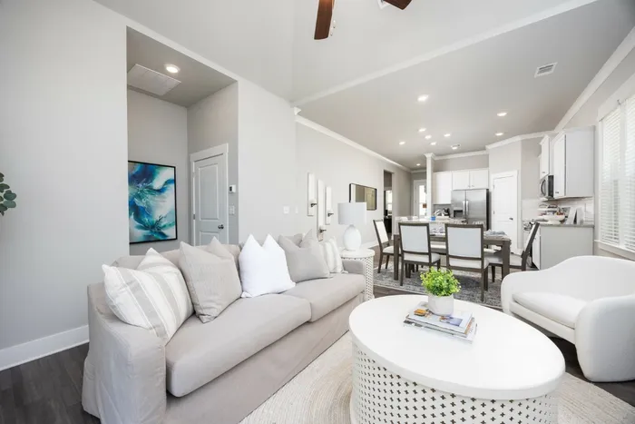 3-Bedroom Homes for Rent in Opelika, AL - Champions Square - Living Room with Luxury Vinyl Plank Flooring, Area Rug, Sofa, Coffee Table, Armchair, High Ceilings, Ceiling Fan, and View of Dining Area and Kitchen.