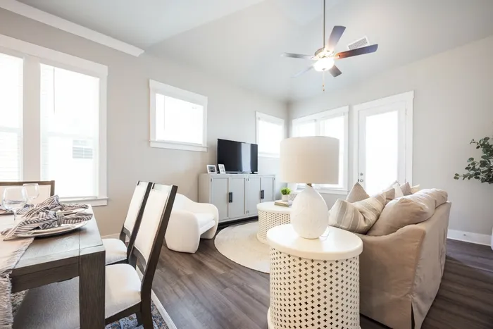Pet-Friendly Houses for Rent in Opelika, AL - Champions Square - Bright Open Living And Dining Area With Large Windows, Ceiling Fan, Wood Style Flooring, Neutral Sofa, And Media Console.