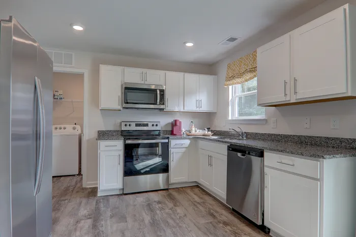 Asheville, NC, Pet-Friendly Townhomes - The Townes at Fountain Park - Chef-Inspired Kitchen with Luxury Vinyl Plank Flooring, Stainless Steel Whirlpool Appliances, Granite Countertops, White Cabinetry, Window, and View of Laundry Laundry Closet.