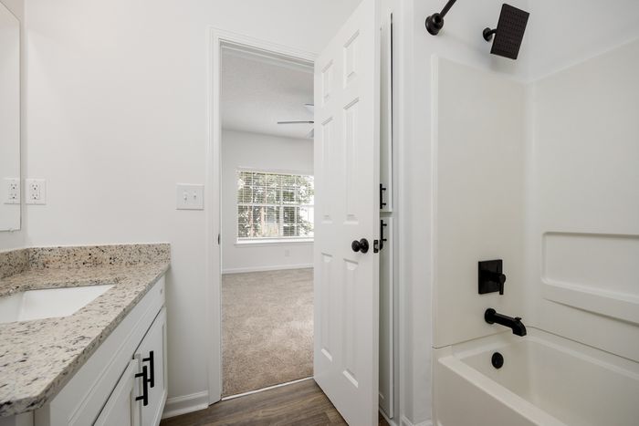 Bathroom eith sink and standard tub with view into an unfurnished bedroom