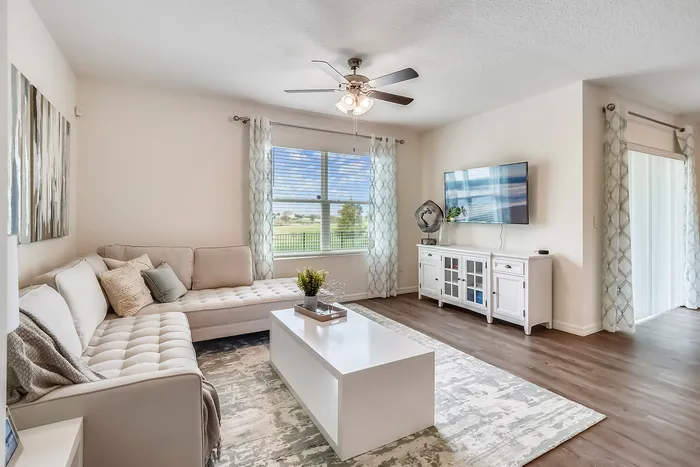 Cozy and elegant living room with a light beige sectional sofa, sleek white coffee table, and large wall-mounted TV.