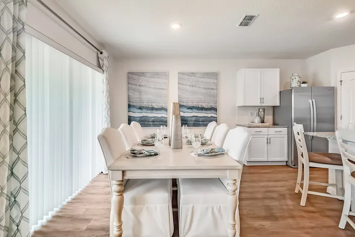 Townhomes Near Asheville Outlets in Fairview, NC - Fairview Meadows - Dining Room Featuring Floor Length Blinds, Wood-Style Flooring, Wall Art, and a Stainless Steel Fridge