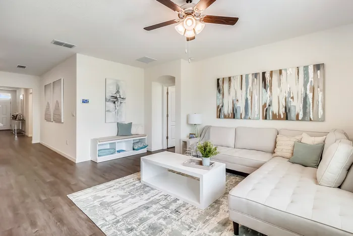 Bright modern living room with elegant decor, featuring a light gray sectional sofa, abstract art, and a ceiling fan.