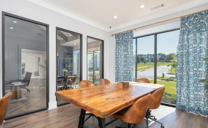 Sunlit conference room with wooden table, leather chairs, and blue patterned curtains overlooking a landscaped garden.