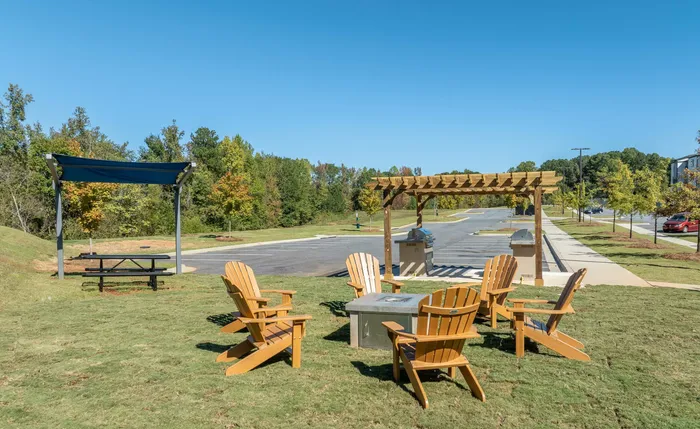 Charming outdoor area with Adirondack chairs and a BBQ grill surrounded by lush greenery.